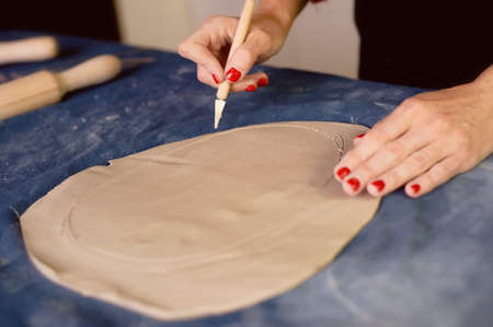 Creative workshop of ceramist. Trimming with a scalpel , creating the form an earthen dish. Workflow