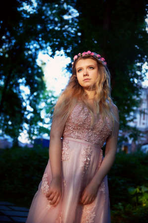 Portrait of a beautiful bride blond girl in pink lace dress ,hair decoration, handmade. Tenderness. Standing in the midst of a dark forest green in the rays of the setting sun. Princessの写真素材