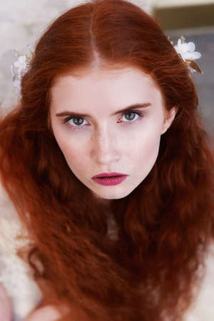 Portrait of a beautiful redheaded girl with long curly hair. Bride. With handmade jewelry on the hair. Hair to the waist. Very long red hair. Big facialの写真素材