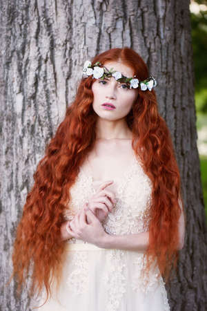 Portrait of a beautiful redheaded girl with long curly hair. Bride. With handmade jewelry on the hair. Hair to the waist. Very long red hair. The average planの写真素材