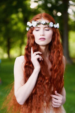 Portrait of a beautiful redheaded girl with long curly hair. Bride. With handmade jewelry on the hair. Hair to the waist. Very long red hair. The average planの写真素材