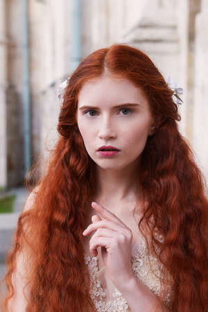 Portrait of a beautiful redheaded girl with long curly hair. Bride. With handmade jewelry on the hair. Hair to the waist. Very long red hair. The average planの写真素材