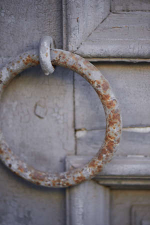 Old vintage grey door with peeling paint and a rusty handle in the form of a ringの写真素材