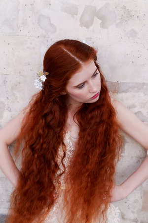Beautiful red-haired girl with long curly hair in the bride, in a long lace dress. A natural beauty.の写真素材