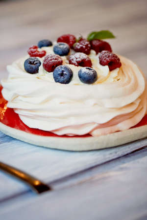Dessert Anna Pavlova with raspberries and blueberries on white wooden surface