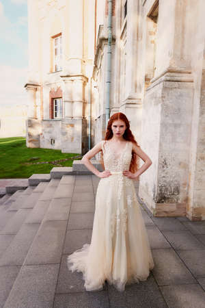Beautiful red-haired girl with long curly hair in the bride, in a long lace dress. A natural beauty.の写真素材