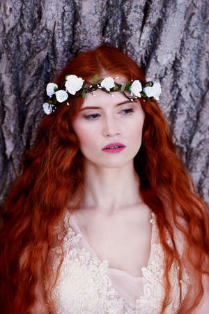 Beautiful red-haired girl with long curly hair in the bride, in a long lace dress. A natural beauty.の写真素材