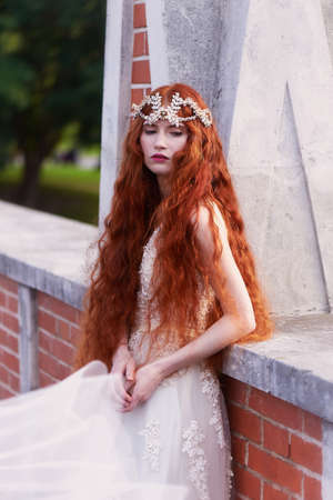 Beautiful red-haired girl with long curly hair in the bride, in a long lace dress. A natural beauty.の写真素材