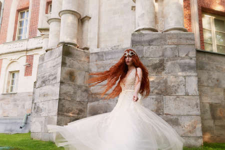 Beautiful red-haired girl with long curly hair in the bride, in a long lace dress. A natural beauty.の写真素材