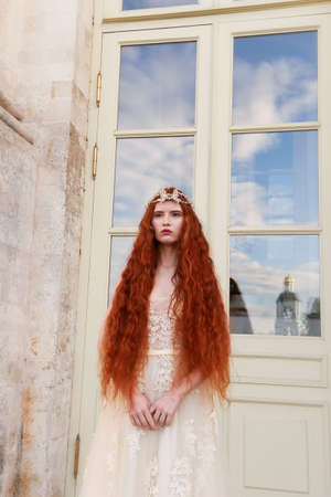 Beautiful red-haired girl with long curly hair in the bride, in a long lace dress. A natural beauty.の写真素材
