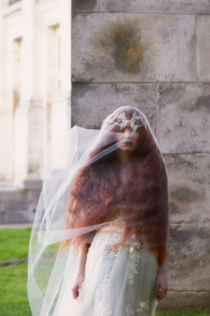 Beautiful red-haired girl with long curly hair in the bride, in a long lace dress. A natural beauty.の写真素材