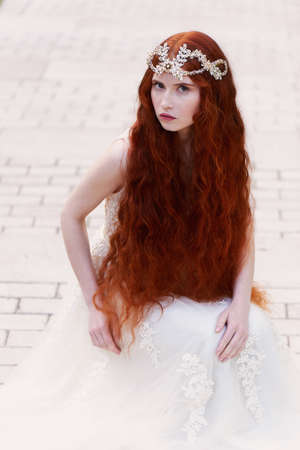 Beautiful red-haired girl with long curly hair in the bride, in a long lace dress. A natural beauty.の写真素材