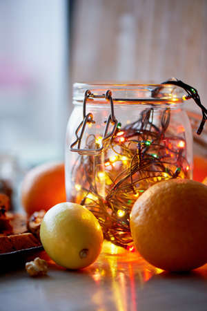 New years table. Garland, glowing in a glass jar. Among the citrusの写真素材