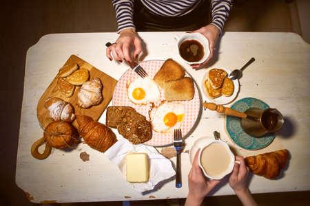Breakfast, view from the top. Toast, coffee, fried eggs. Hands of two girls