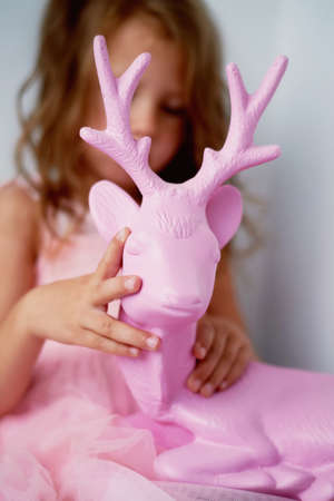 A lovely little girl 4 years old in a pink dress plays with pink deer. The atmosphere of childhoodの写真素材