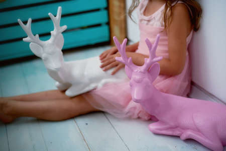 A lovely little girl 4 years old in a pink dress plays with pink deer. The atmosphere of childhoodの写真素材