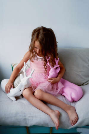 A lovely little girl 4 years old in a pink dress plays with pink deer. The atmosphere of childhoodの写真素材