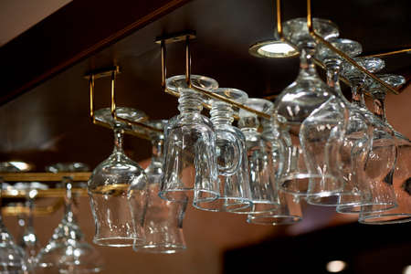Wine glass glasses hang on the holders above the bar. The atmosphere of the evening pub, restaurant, cafeの写真素材