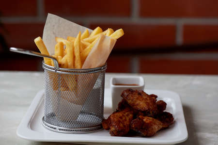 Chicken wings with sauce and fries in a metal stand on parchment paperの写真素材