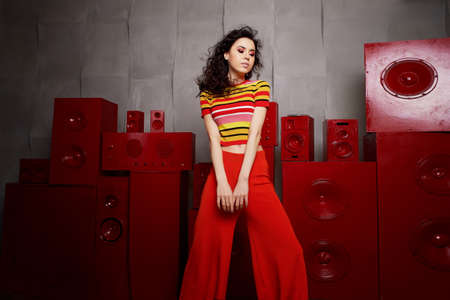 Studio fashion shooting. The girl in a bright outfit, top and pants flared in red and orange colors....