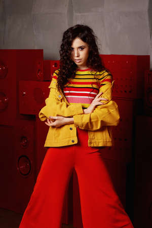 Studio fashion shooting. The girl in a bright outfit, top and pants flared in red and orange colors....
