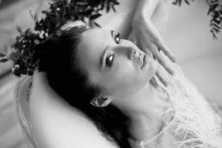 Bright Studio.Delicate and sensual atmosphere of peace and tranquility. Relaxation. Portrait of a beautiful girl with plump lips, graceful thin wrists, lying in the bath.の写真素材
