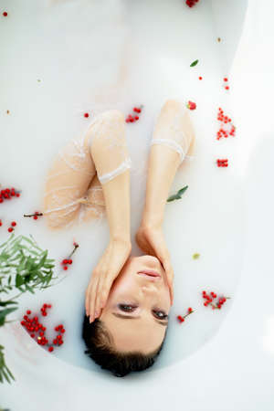 Bright Studio.Delicate and sensual atmosphere of peace and tranquility. Relaxation. Portrait of a beautiful girl with plump lips, graceful thin wrists, wet hair. Lying in a milk bath with Rowan.の写真素材