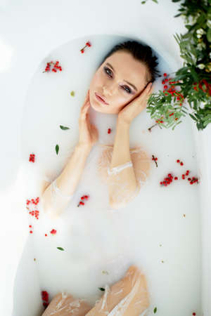Bright Studio.Delicate and sensual atmosphere of peace and tranquility. Relaxation. Portrait of a beautiful girl with plump lips, graceful thin wrists, wet hair. Lying in a milk bath with Rowan.の写真素材