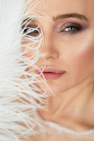 Bright Studio.Delicate and sensual atmosphere of peace and tranquility. Relaxation,Portrait of a beautiful girl with plump lips, graceful thin wrists, with a white fluffy feather. Cats eyeの写真素材