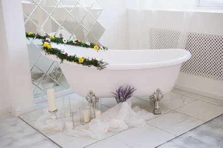 The luxurious bathroom is decorated with flowers and candles. With a big mirror.