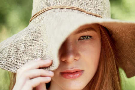 A sophisticated red-haired girl in a simple linen dress, in a light wide-brimmed hat. Model look. Natural beauty. Artistic portraitの写真素材