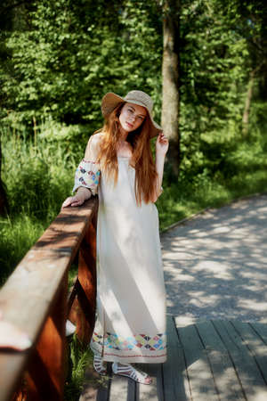A sophisticated red-haired girl in a simple linen dress, in a light wide-brimmed hat. Model look. Natural beauty. Artistic portraitの写真素材