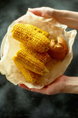 A plate with boiled corn cob, on parchment paper, in a plate. On a dark background, in a rustic style. vegetarian simple foodの写真素材