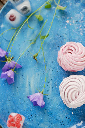 The marshmallow on a blue sky plate. Light dessert. Delicate wildflowers. And frozen in the ice berriesの写真素材