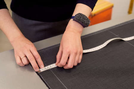 The seamstress lays out the fabric for cutting using inches. Hands in shot.