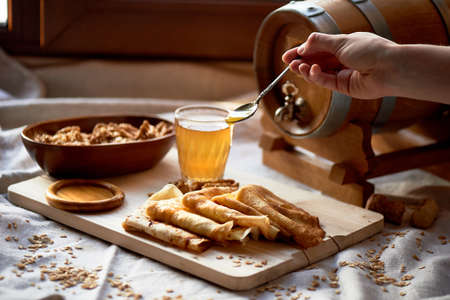 Mead and pancakes. Russian dish for Shrove Tuesday. Farewell to winter. The hand in the frame. Honey from a spoon dripping on pancakesの写真素材