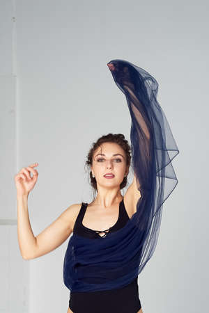 A slender gymnast in black tights dances with a blue chiffon that develops. Aesthetics of dance