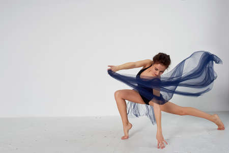 A slender gymnast in black tights dances with a blue chiffon that develops. Aesthetics of dance