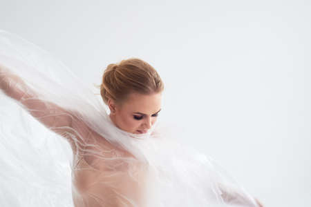 Gymnast dancing with a transparent film on a white wall and floor. Grace and healthy lifestyle.の写真素材