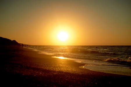 Sea Golden sunset. Waves run on the sandy shore. Silhouettes of people walking along the shore.の写真素材