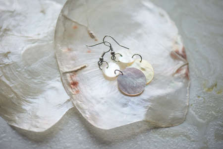 Sea collection on grey marble background.Seashell and mother-of-pearl earrings. Summer jewelry.Mother-of-pearl plates and pearl earrings.の写真素材