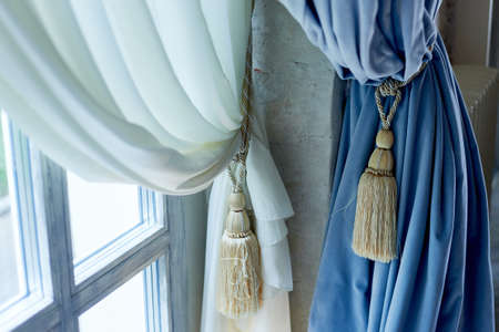 Brush with threads on the blue curtains. Light wood window. Classical interior.の写真素材