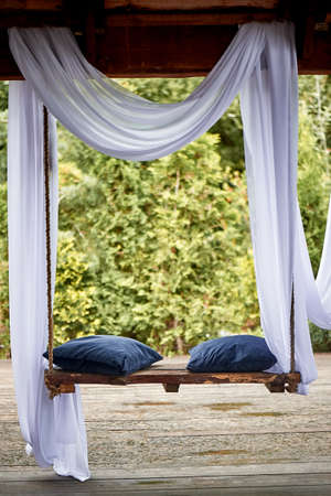 Wooden swing in the garden, with blue soft cushions. A cozy place to relaxの写真素材