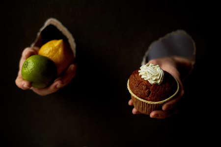 Collage .Hand in the hole of the paper. Holds a cupcake, and a lemon. Against the sweet fruit. Diet or gluttony. Trend, place for text.の写真素材