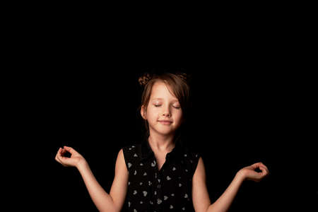 A girl of 6 years on a black background. Meditation and calm, in quarantine and distance learning.の写真素材