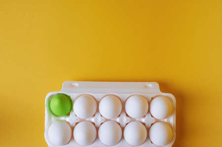 Packaging with a dozen eggs on a yellow background. One egg is painted green. Preparing for Easter.の写真素材