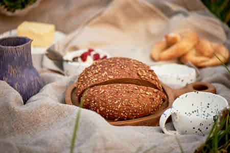 Picnic in nature. Fresh bread with cereals on a wooden board, linen tablecloth, pottery. Eco-style.