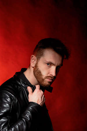 A brutal man on a dark background in the light of a red lamp. Black leather jacket