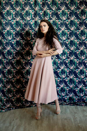 Slender girl in a pink dress on the background of patterned Wallpaper. Style, fashion and beauty.