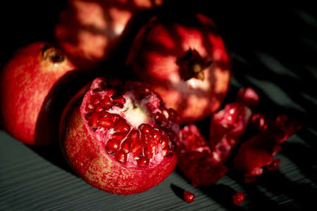 Pomegranate on a black background. Shadow from the suns window. Whole and seeds. Vitamins in hot climates.の写真素材